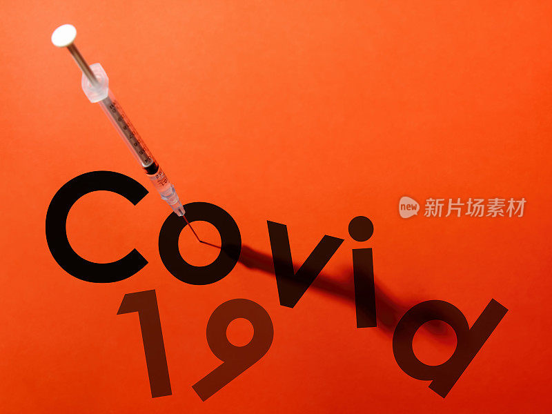 注射器上的针头穿过单词COVID-19 (COVID-19)中的字母“o”的中心。